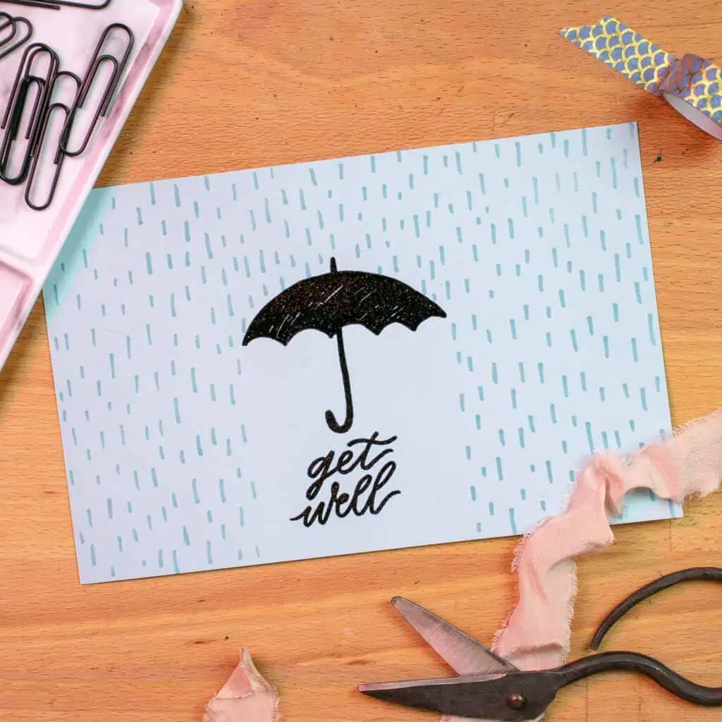 A Get Well card with an embossed illustration. The illustration is a black umbrella in a blue rainstorm, with the words get well written below.