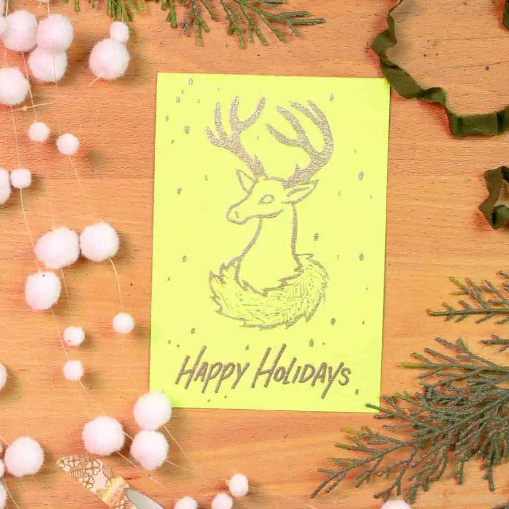 A yellow holiday card that has a deer illustration embossed.